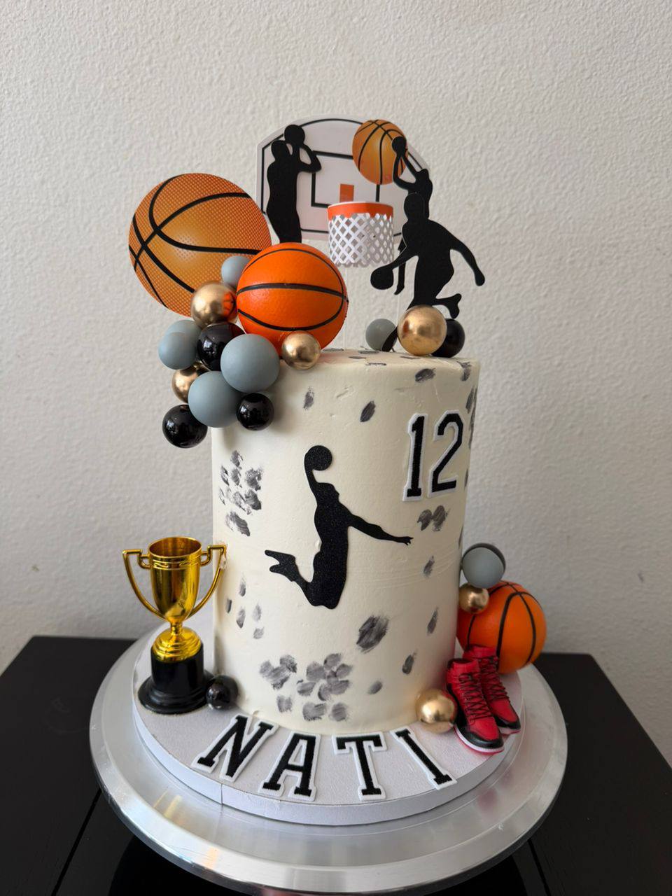 Cream cake with basketball player silhouettes, gold trophy, red sneakers, and orange balloon clusters, name Nati, age 12