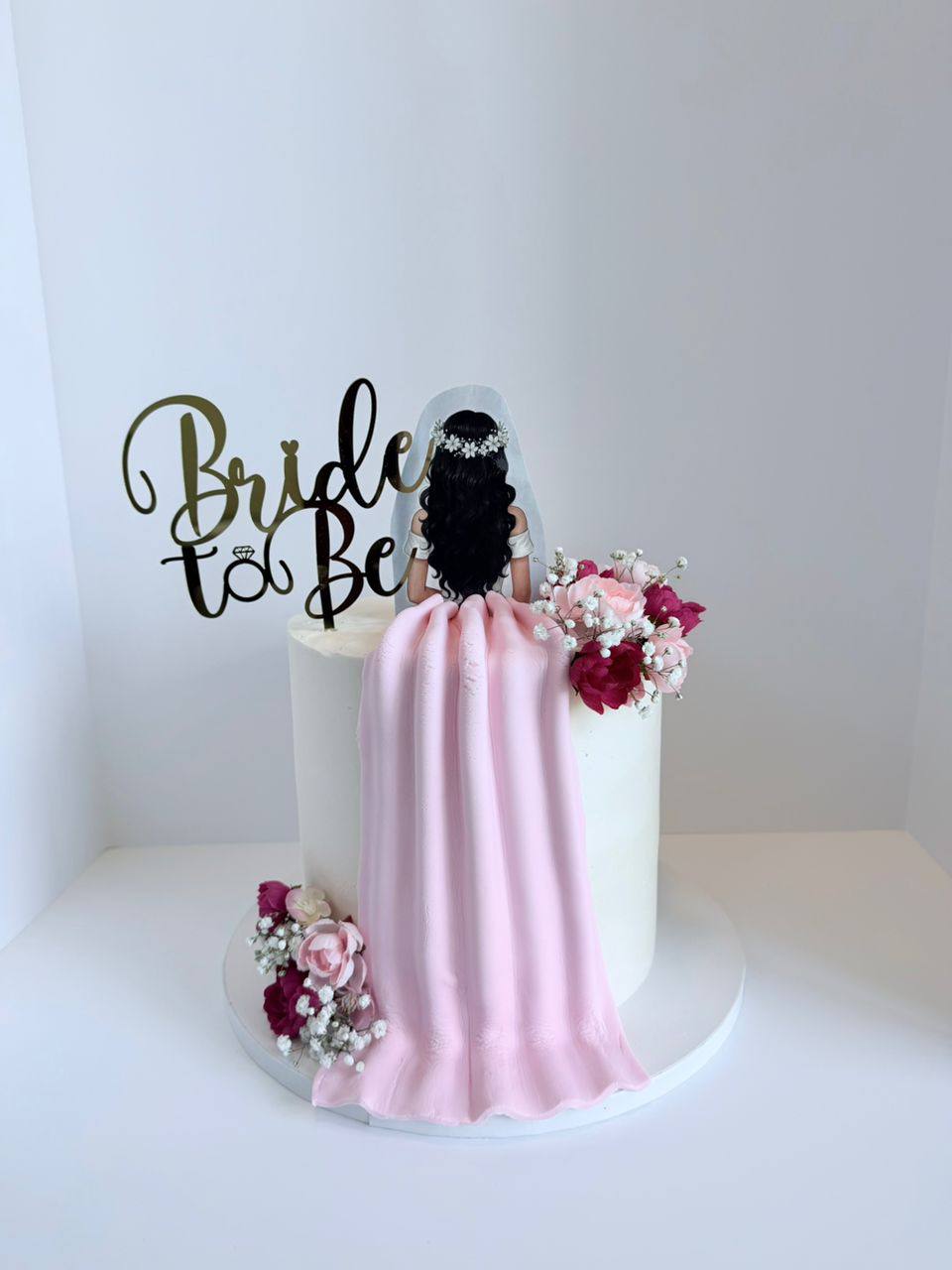 White cake with a fondant bride figure in a flowing pink gown and fresh floral accents