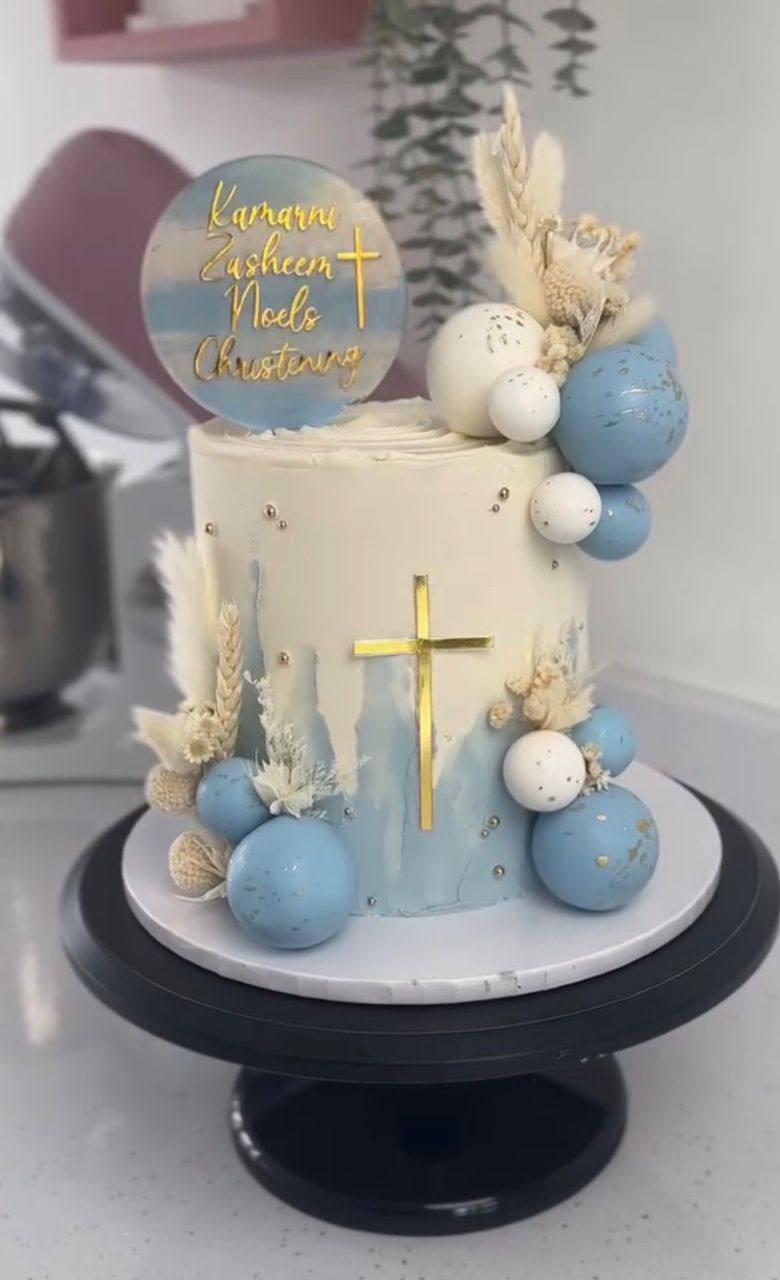 Ivory and dusty blue watercolor cake with a gold cross, blue and white spheres, and dried florals, christening topper