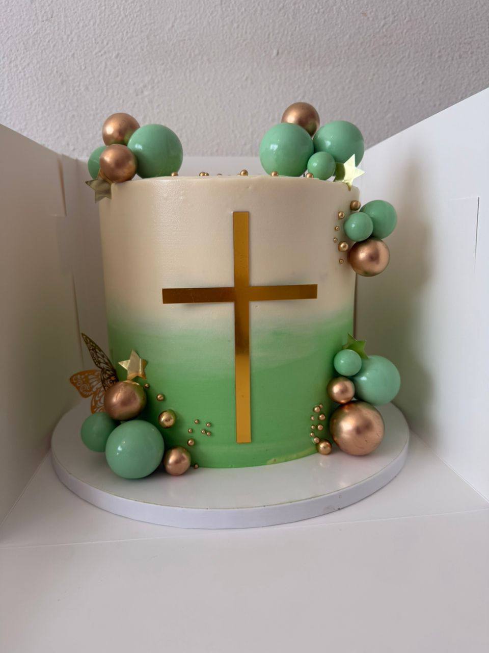 White to green ombre christening cake with a gold cross, mint and rose-gold spheres, gold pearls, and gold butterfly