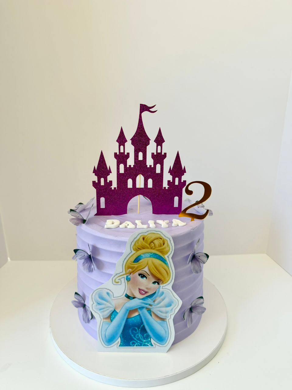 Lavender cake with a purple glitter castle topper and printed Cinderella image, fabric butterflies, name Daliya, age 2