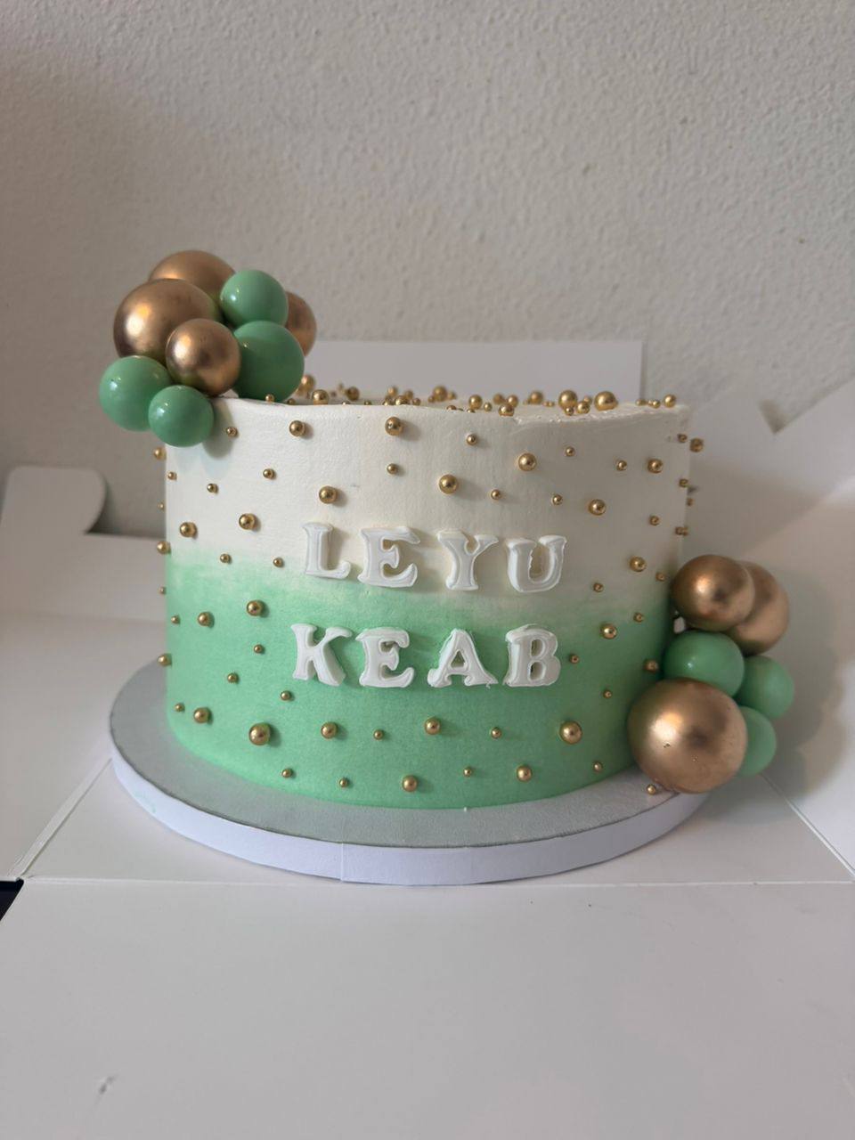 White to mint green ombre cake covered in gold pearls with green and gold spheres, 'Leyu Keab' lettering