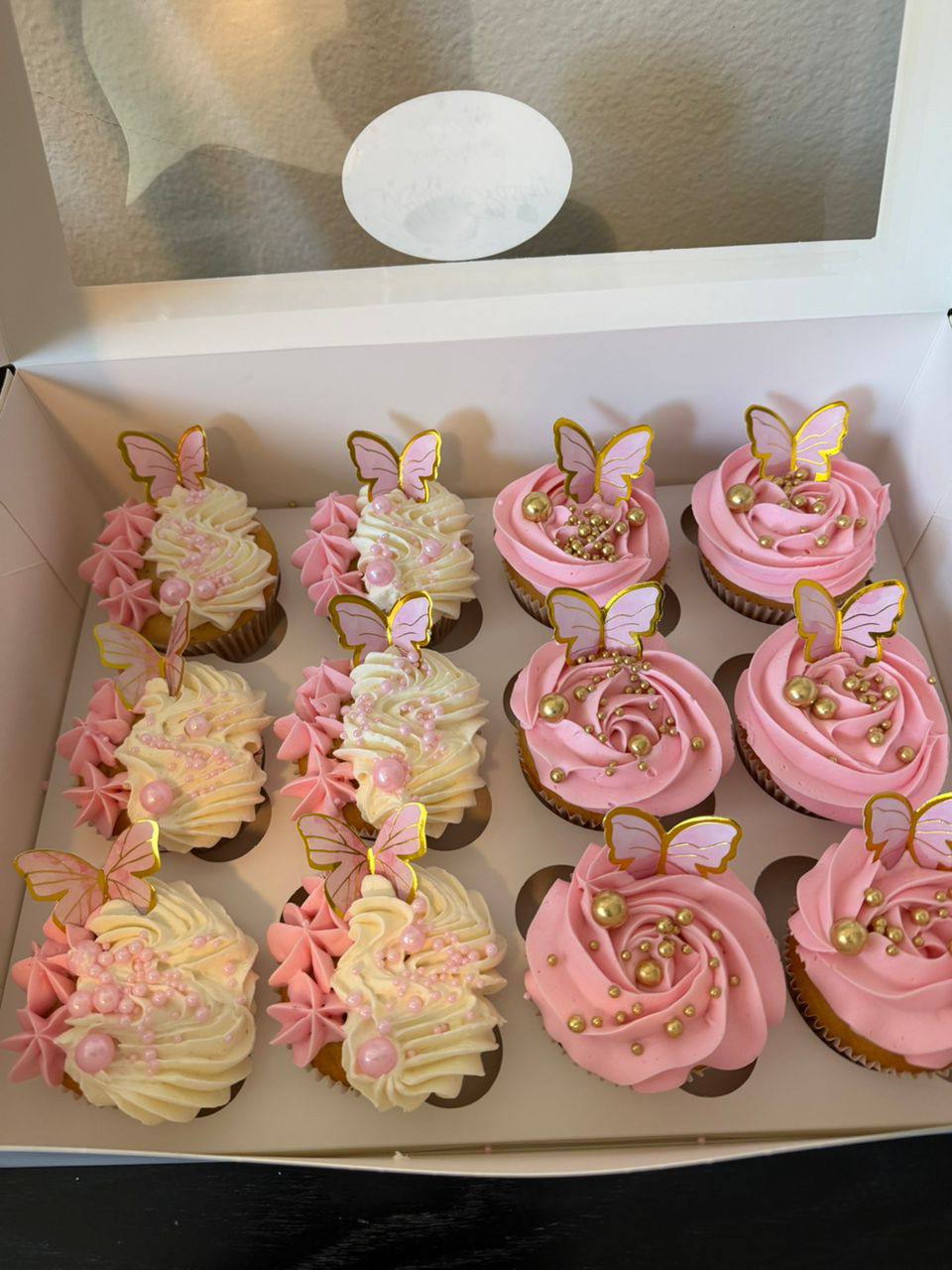Boxed dozen of pink and vanilla rosette cupcakes with gold-rimmed butterfly toppers and pearl accents