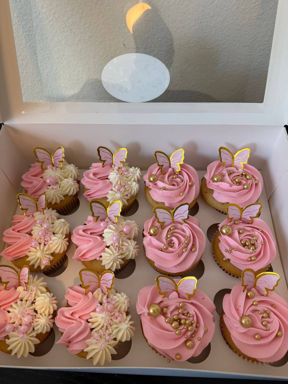 A dozen pink and cream swirl cupcakes topped with gold-edged butterflies, gold pearls, and pink beading