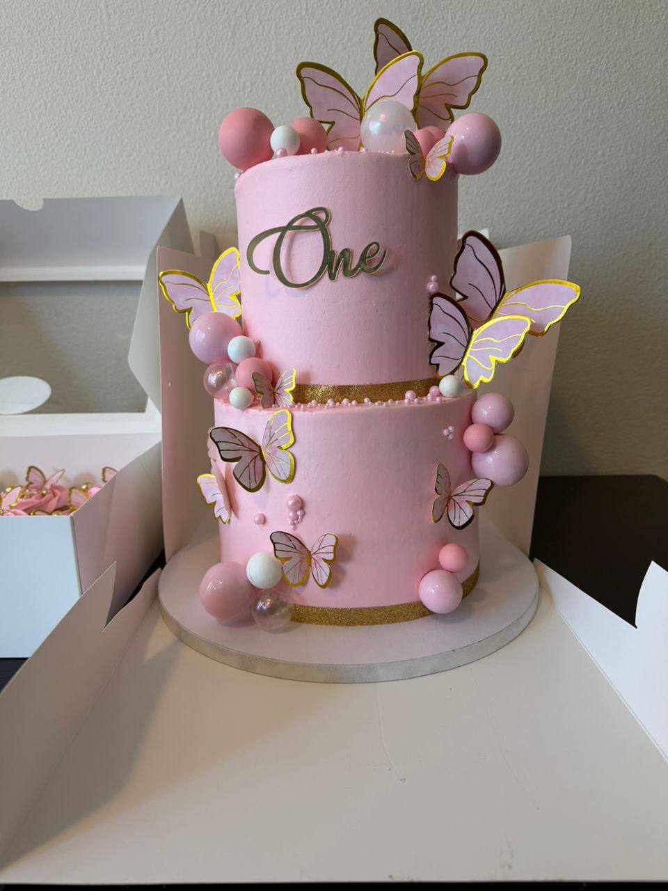 Pink two-tier first birthday cake with gold-edged butterflies and pastel spheres