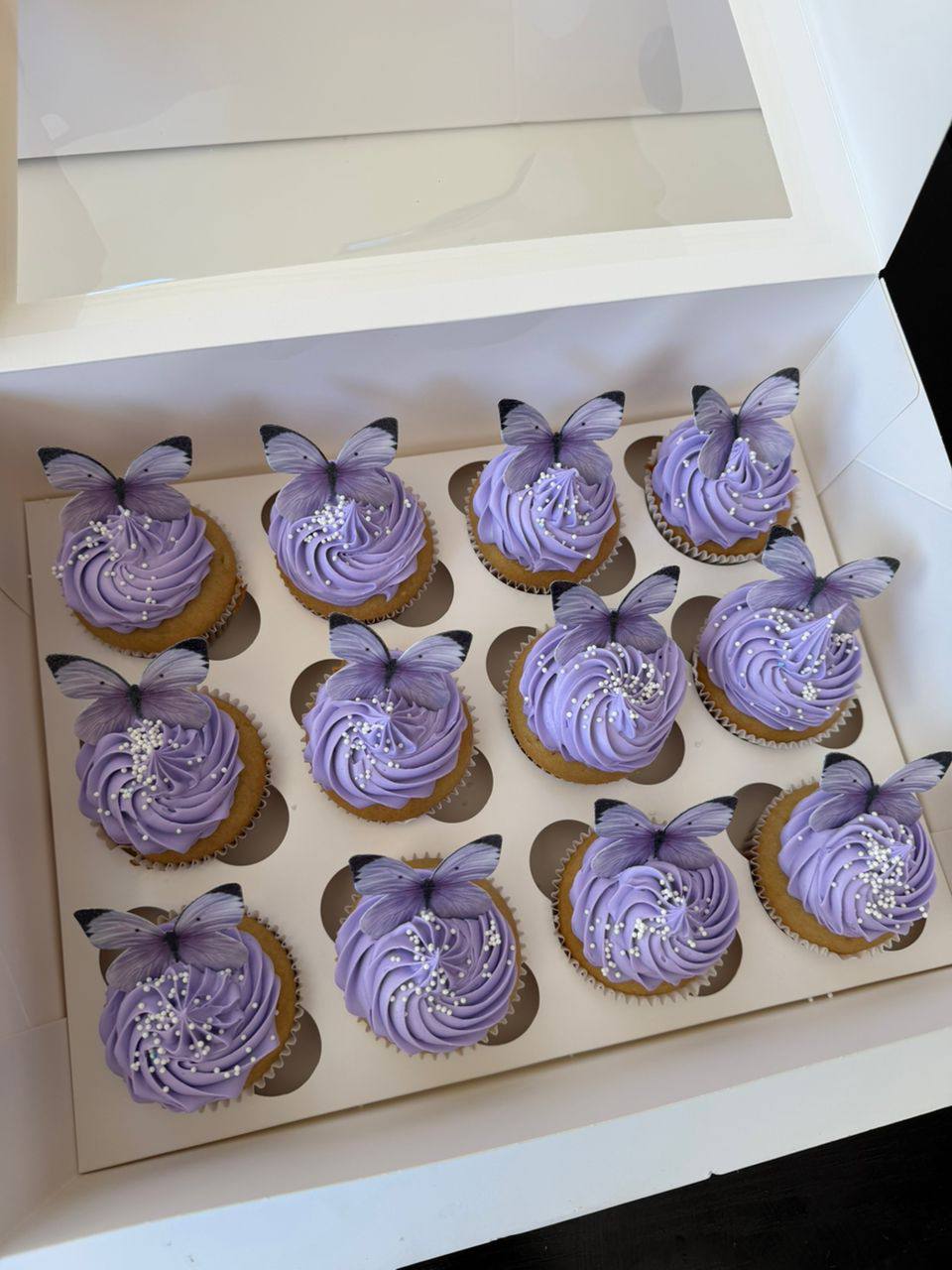 A dozen lavender swirl cupcakes topped with edible butterflies and white pearl sprinkles