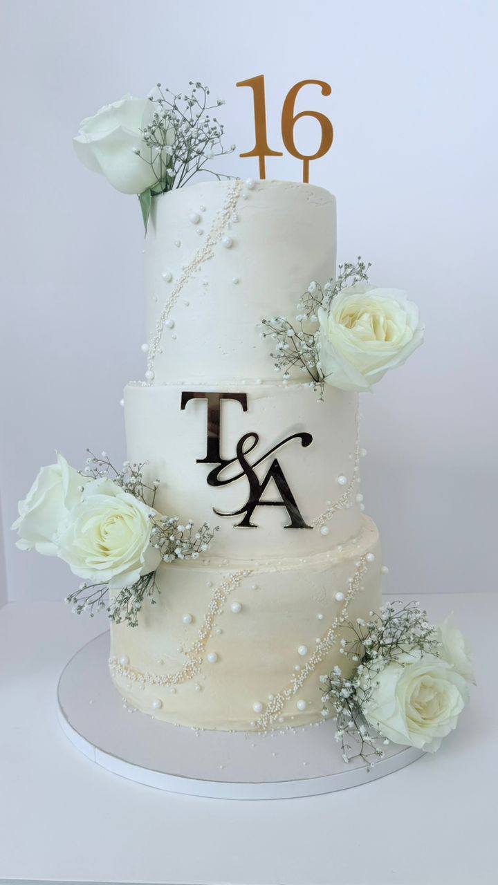 Three-tier ivory cake with pearl garlands, white roses, and a gold 16 topper with T&A monogram